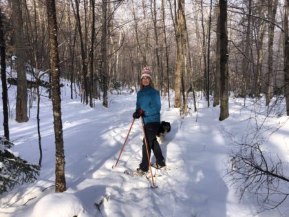 winter, snow woman on snowshoes smiling and black and white dog, in woods