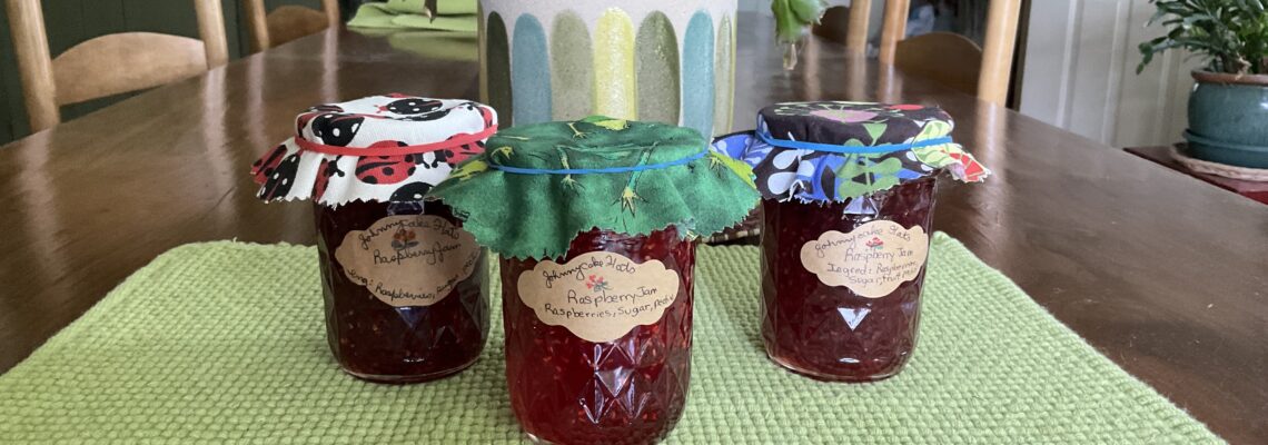 3 jars raspberry jam on green placemat, wood table