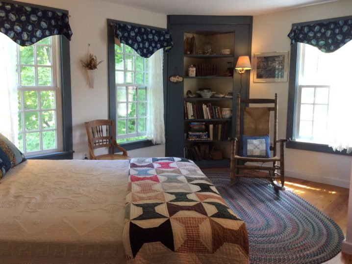 Train room, bed, spool quilt, braided rug, corner bookcase, rocking chair, 3 windows